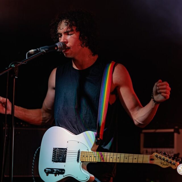 Alex Hutin chante sur scène lors d'un concert de LAST RAINBOW à l'altherax. Il laisse sa guitare électrique de côté le temps de placer ses bras en W