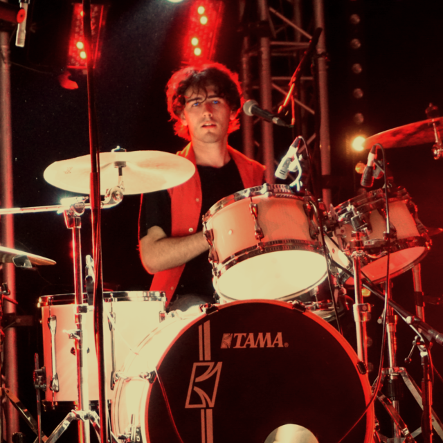 Raphaël Meyer le célèbre batteur de LAST RAINBOW joue de la batterie lors d'un concert aux vinestivales à Vinon-sur-Verdon. L'image est plutôt rouge et les yeux bleus du batteur ressortent avec éclat